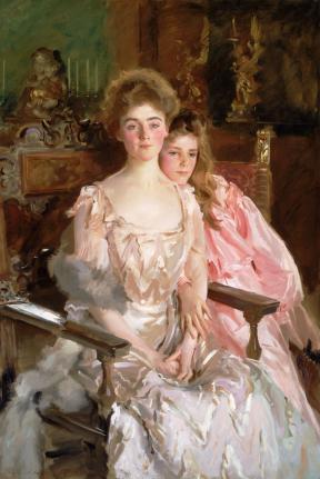 A woman and her daughter wear flowing gowns and sit close to one another on ornate chairs. 