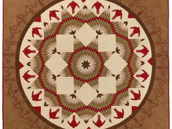 Quilt of browns, reds, and whites with a circle with figures and star shaped patterns