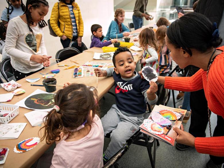 A young boy holds up his artwork at an art-making table