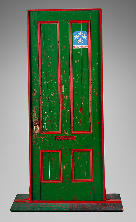 A bullet hole–riddled green door with red trim and a blue sticker reading "USA Approved."
