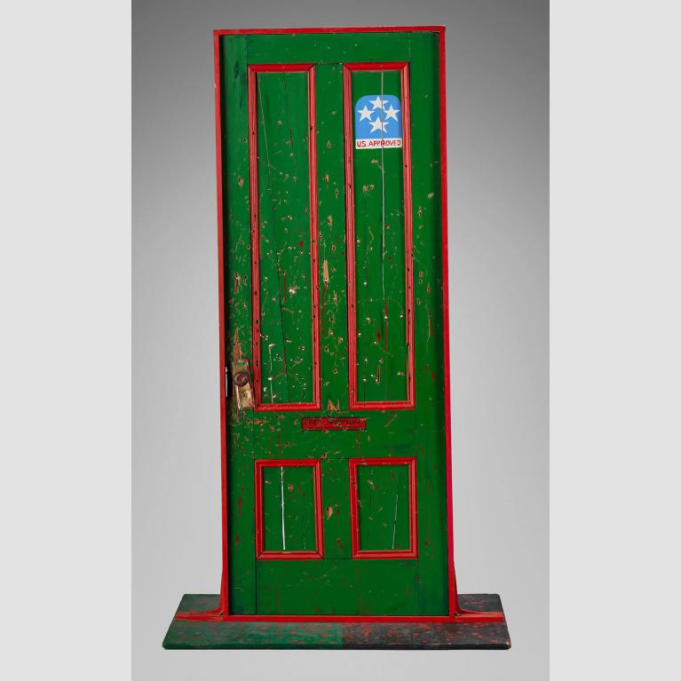 A bullet hole–riddled green door with red trim and a blue sticker reading "USA Approved."