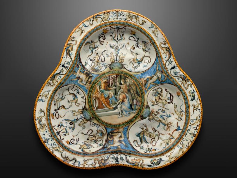 A trilobed, earthenware basin with a white background and a central medallion surrounded by grotesque figures 