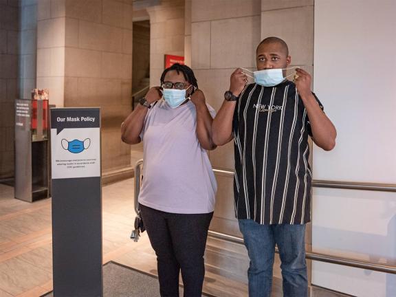 Two visitors putting on masks inside the Museum