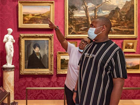 Two visitors looking up at paintings in the Salon gallery, one visitor pointing upwards