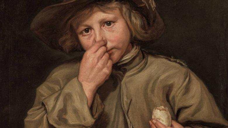 A boy wearing a hat pinches his nose with his right hand.