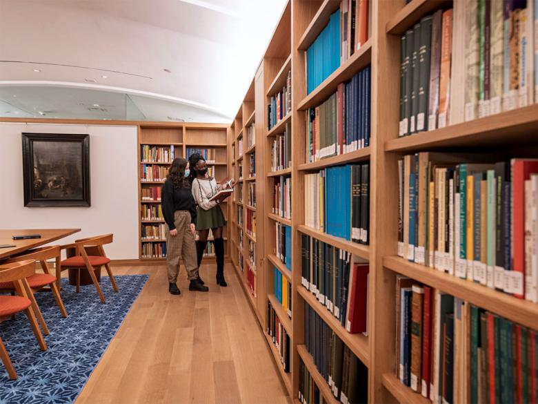Two young people stand in front of bookshelves and flip through a book.
