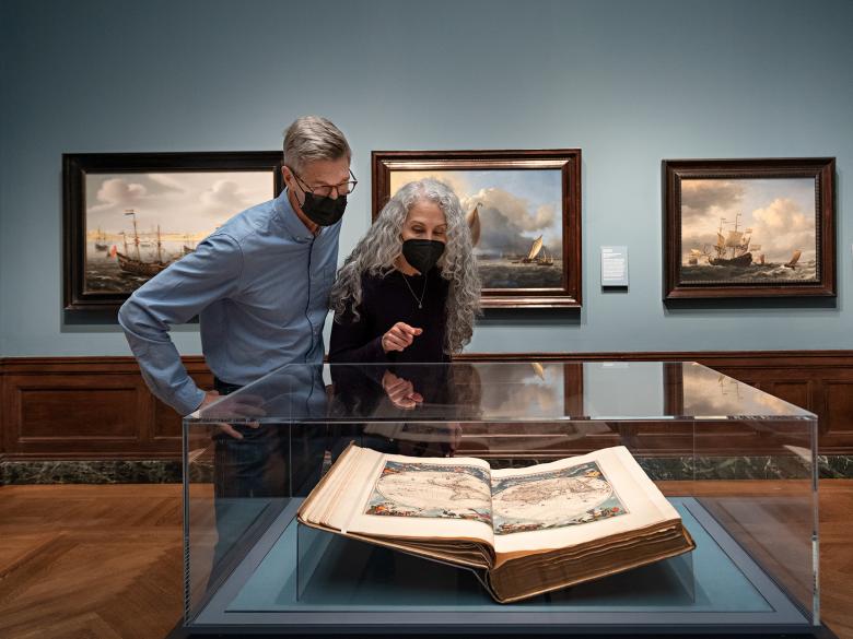 Two visitors look at an open book revealing a map.