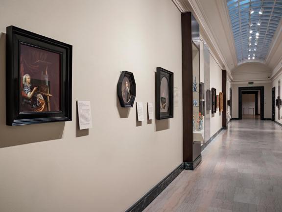 A long corridor with framed works of art on white walls.