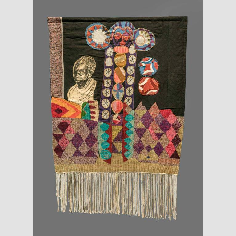 A hanging, mixed textile media, rectangular banner with tassels that depicts different shapes and figures. 