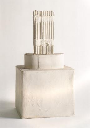 A sculpture of bundled sticks placed on top of a cylinder sat atop a box. 