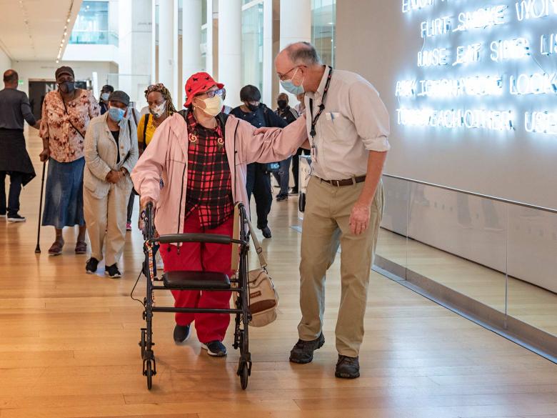 A woman with a walker and a tour guide engage in discussion ahead of a small group who stroll through the contemporary art wing