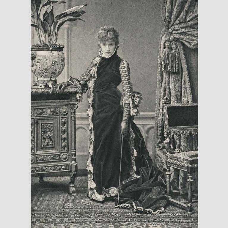 A photo of a woman standing in a long velvet gown and leather gloves. 