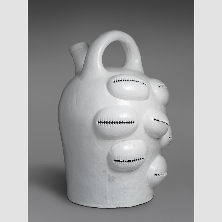 A white glazed stoneware jug with a handle on top and seven adornments that resemble puka shells.