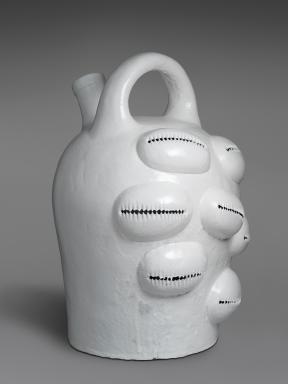 A white glazed stoneware jug with a handle on top and seven adornments that resemble puka shells.