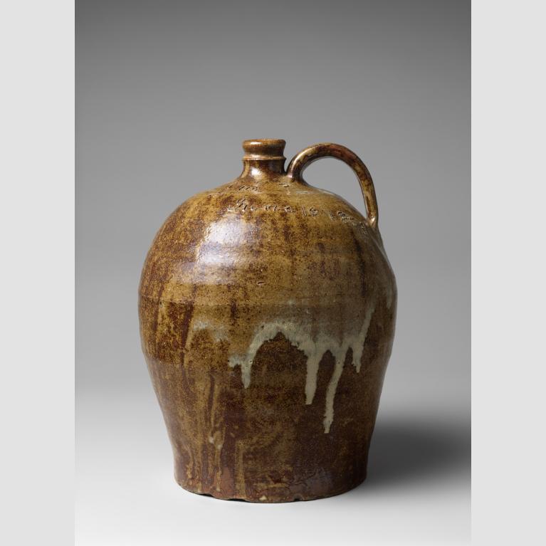 A large, clay jug of brown hues with white drips, a handle, and small opening.