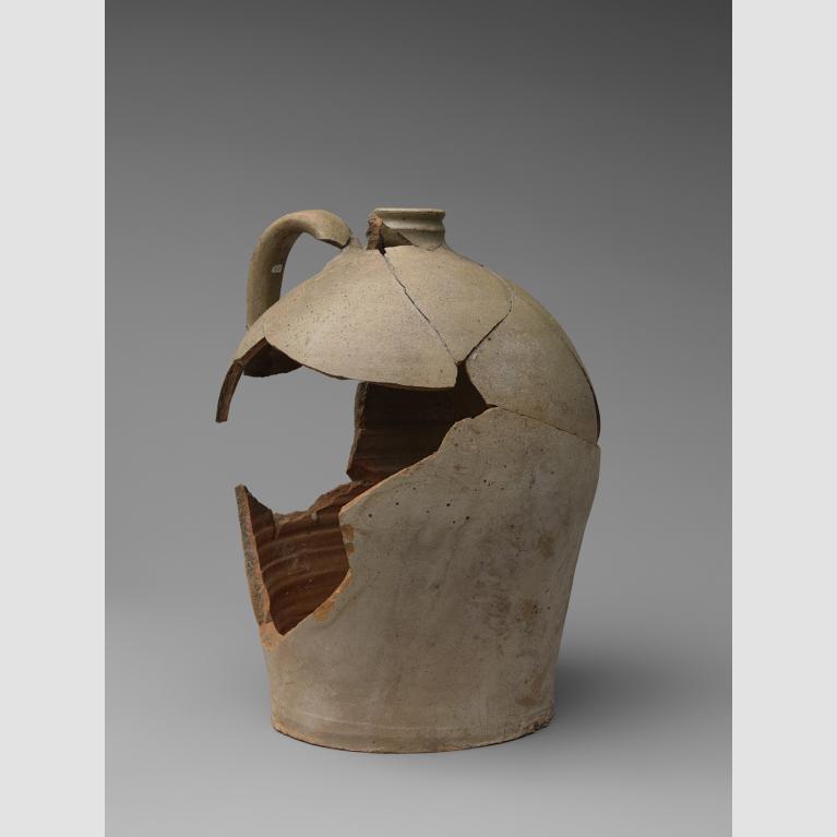 A cracked, reconstructed stoneware jug with handle and a large hole in its side.