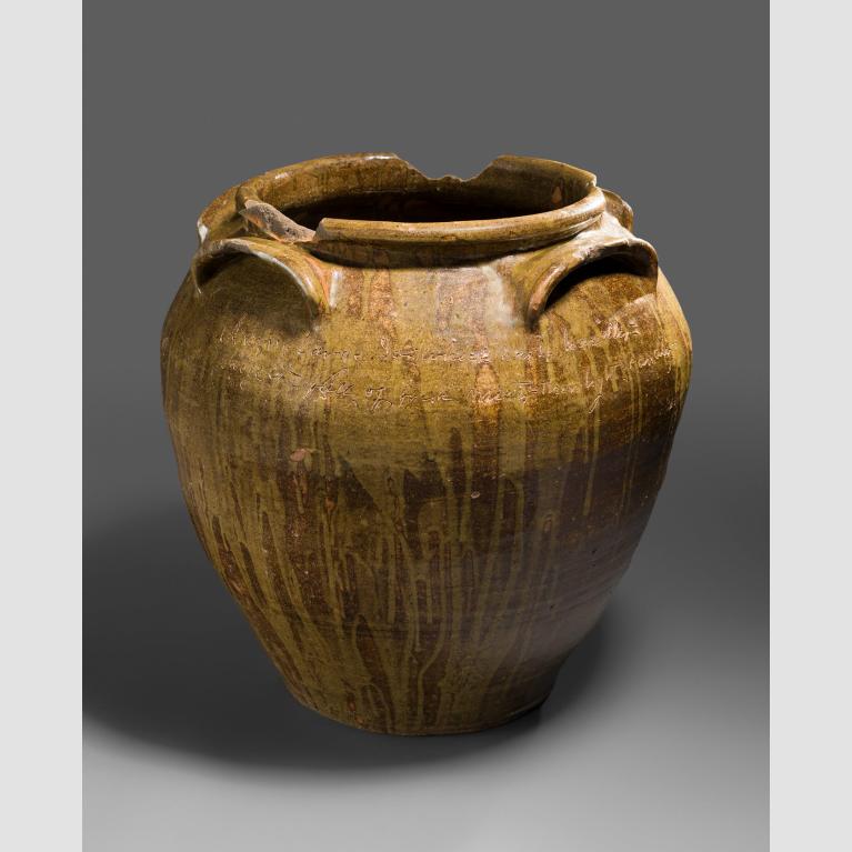 A light orangey-brown jug engraved with text and adorned with a large opening and three handles.