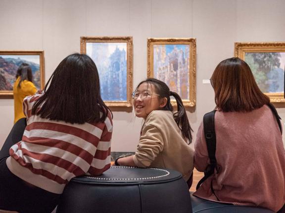 Three visitors chatting on a round couch in Impressionism gallery