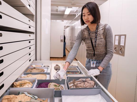 An MFA Pathways Intern wearing white gloves opens a drawer of purses in the Conservation studio.