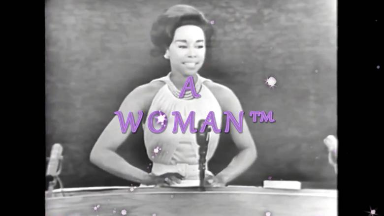 A woman in a gown with arms akimbo stands in front of three microphones.