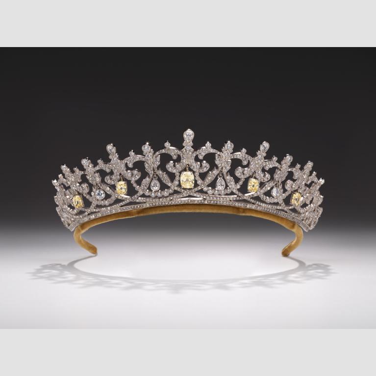 An ornate tiara made of silver and clear Swarovsky crystals with touches of yellow .