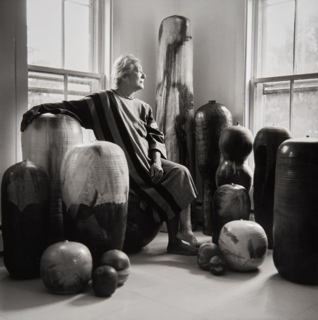 Artist Toshiko Takaezu sits among her works of pottery and looks out the window.