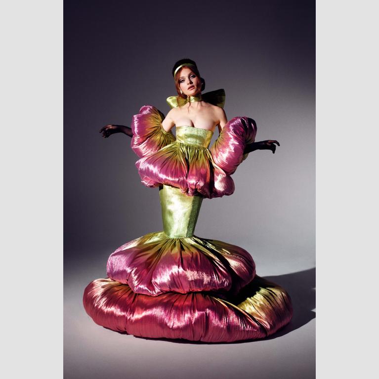 A model poses in a pink and green dress that poofs out at the mid-arms, waist, and feet.