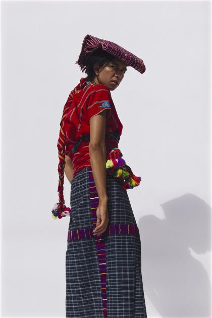 Print depicting a person in an ornate red outfit stands with their back to the camera and looks over their shoulder.