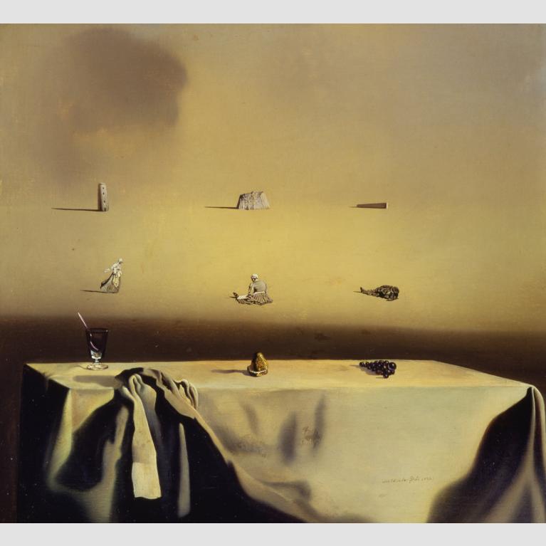 In the foreground, a group of grapes, a spoon in a glass, and a gold object sit atop a table covered in a scrunched white tablecloth; the background is dotted with small women and stone structures. 