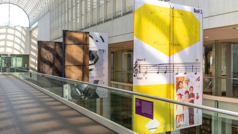Three colorful banners hang beside a catwalk in a light-filled galleria.