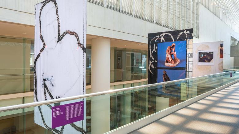 Three colorful banners hang beside a catwalk in a light-filled galleria.