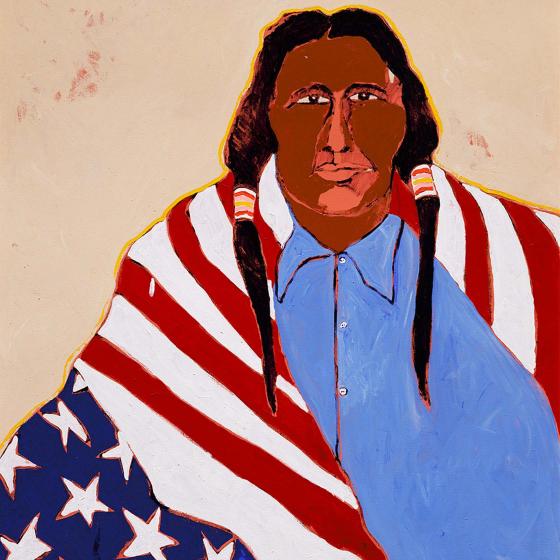 A Native American man in a blue button-down shirt stares straight forward with an upside-down American flag draped over his shoulders.