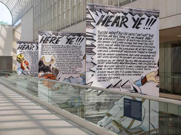 Three large banners hung in Linde Family Wing, featuring text underneath "Hear Ye" headings on each banner and drawings of a town crier on horseback ringing bell