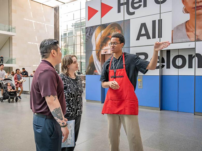 MFA Ambassador in red apron giving directions to two visitors in Shapiro Family Courtyard