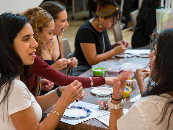 Young adults sitting around art making table, threading beads of various shapes and colors