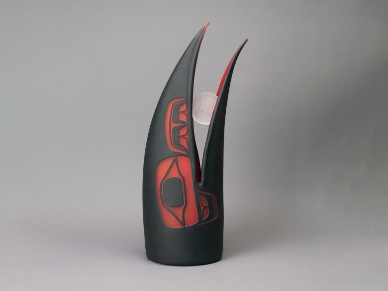 A stylized raven head holding a round piece of sand-blasted glass in its beak.