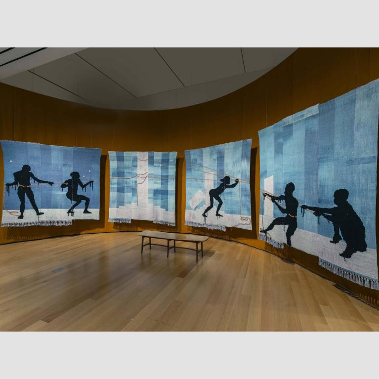 A four-panel tapestry of five silhouetted figures pulling on a rope or a chain. 