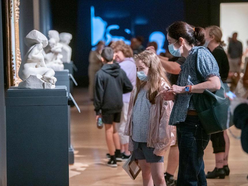 Parent and child looking at small sculpture of reclining figure in gallery