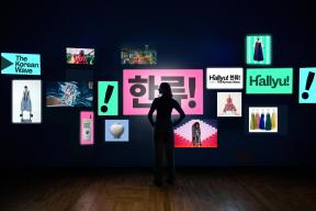 A woman stands in front of a video wall with 15 screens displaying different graphics and images that relate to "Hallyu! The Korean Wave."