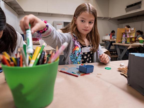 Young student reaches for drawing supplies in classroom (SAC)