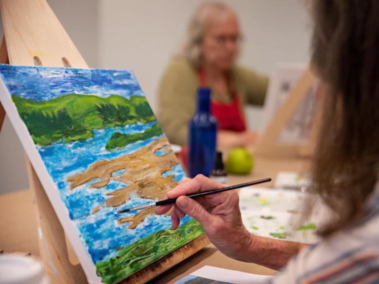 Adult student paints landscape from table top easel (SAC)