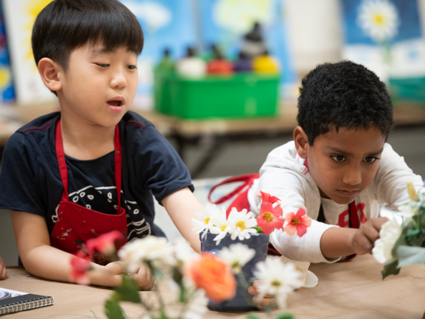 two kids sitting at table, with small flower pots in front of them